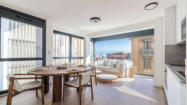 Ein modernes Wohnzimmer mit einem Holzesstisch, bequemen Sitzgelegenheiten, einer Couch und Blick auf die Stadt durch große Fenster.