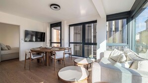 Ein modernes Wohnzimmer mit Essbereich, großen Fenstern und einer Couch.