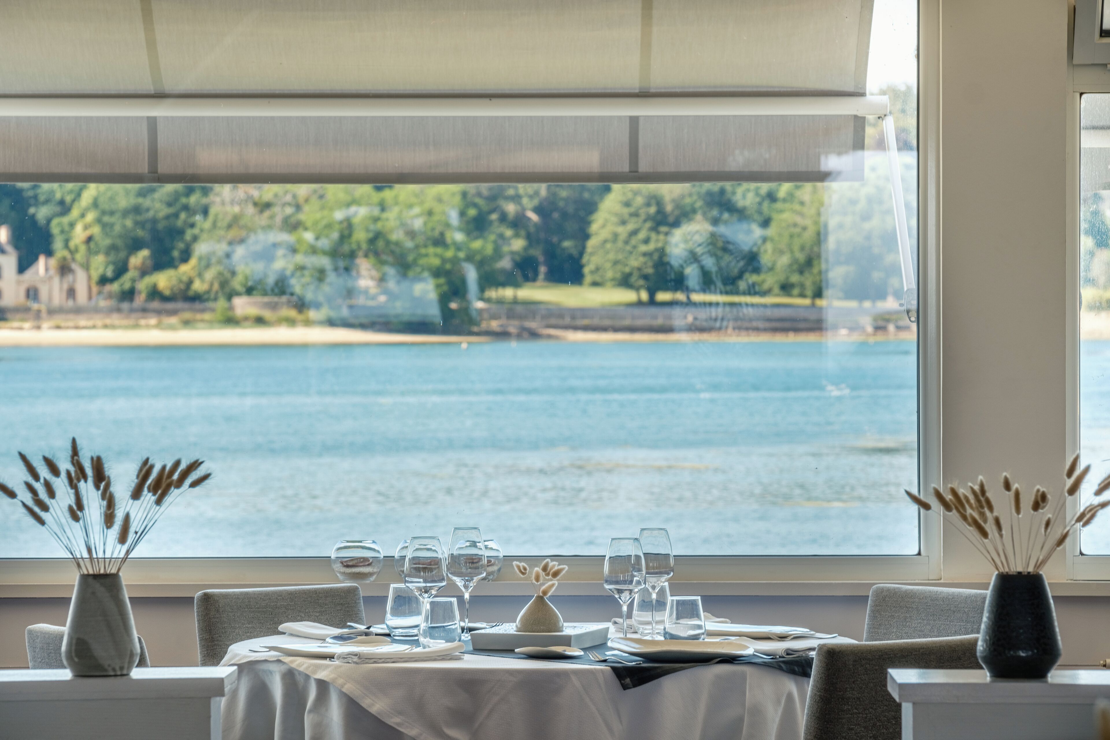 Une table à manger dressée pour deux personnes, avec vue sur un lac et des arbres.