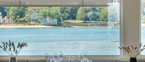 Une table à manger dressée pour deux personnes, avec vue sur un lac et des arbres.