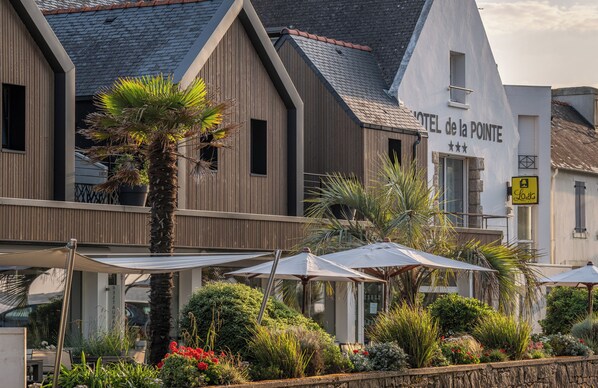 A hotel with a modern facade, outdoor seating with umbrellas, and a well-maintained garden area. - Hôtel de la Pointe du Cap Coz (Fouesnant)