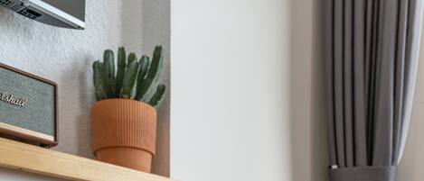 Uma mesa de madeira com uma cesta de vime, uma planta cacto e um alto-falante em uma prateleira.