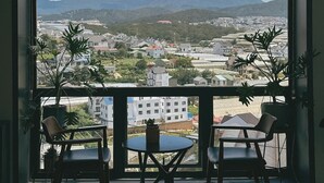 A balcony with two chairs and a table, overlooking a cityscape with mountains in the distance. - View Home Da Lat (Xuan Truong - Da Lat)