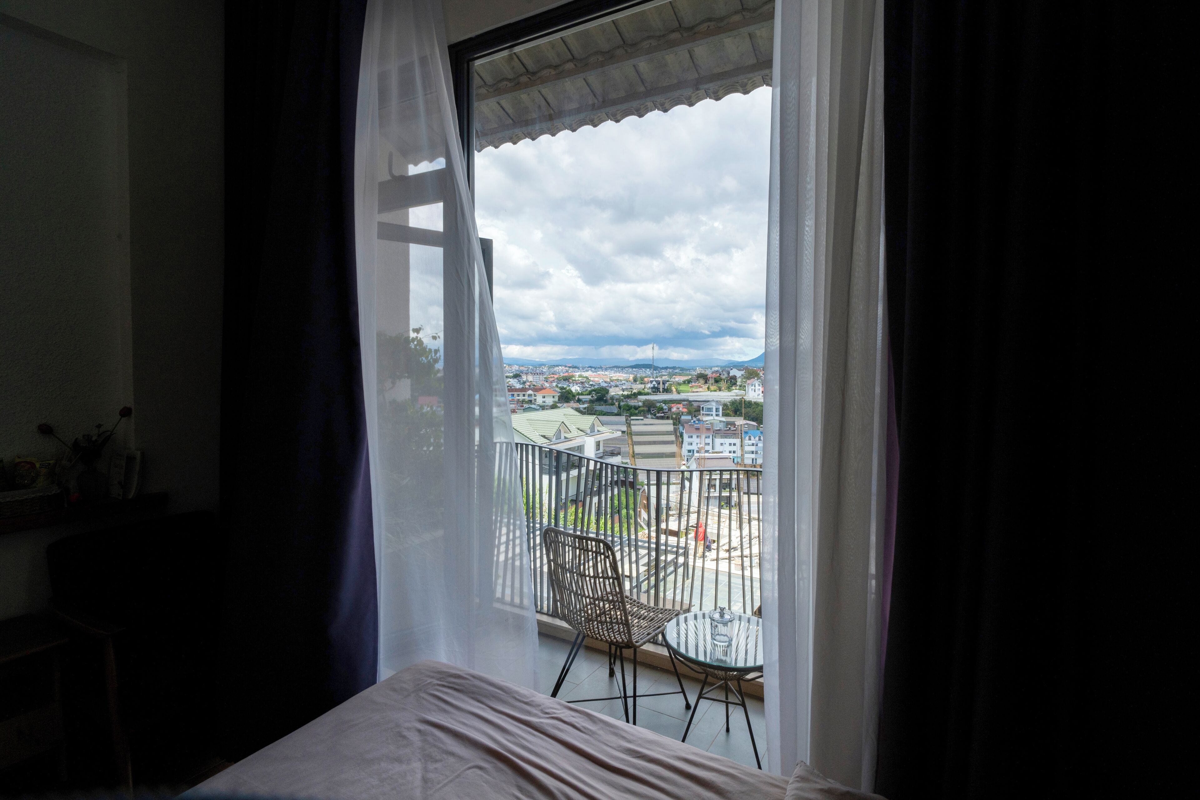 Une chambre avec un lit, une chaise et un balcon donnant sur un paysage urbain.