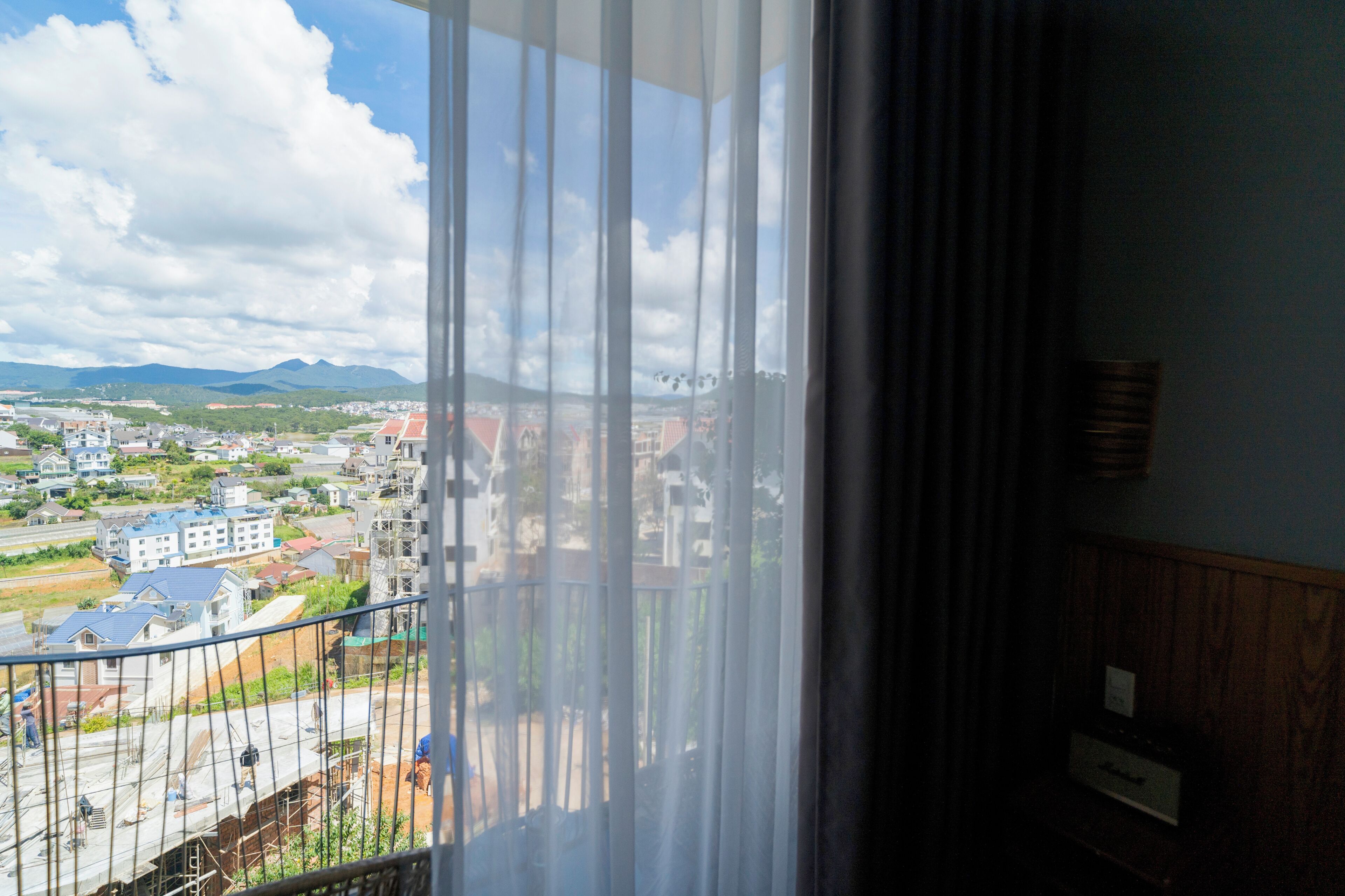 Vista desde una ventana con cortina, que da a una zona residencial con casas y una cadena montañosa distante.