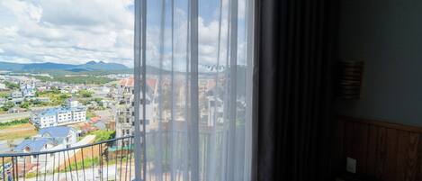 Vista desde una ventana con cortina, que da a una zona residencial con casas y una cadena montañosa distante.