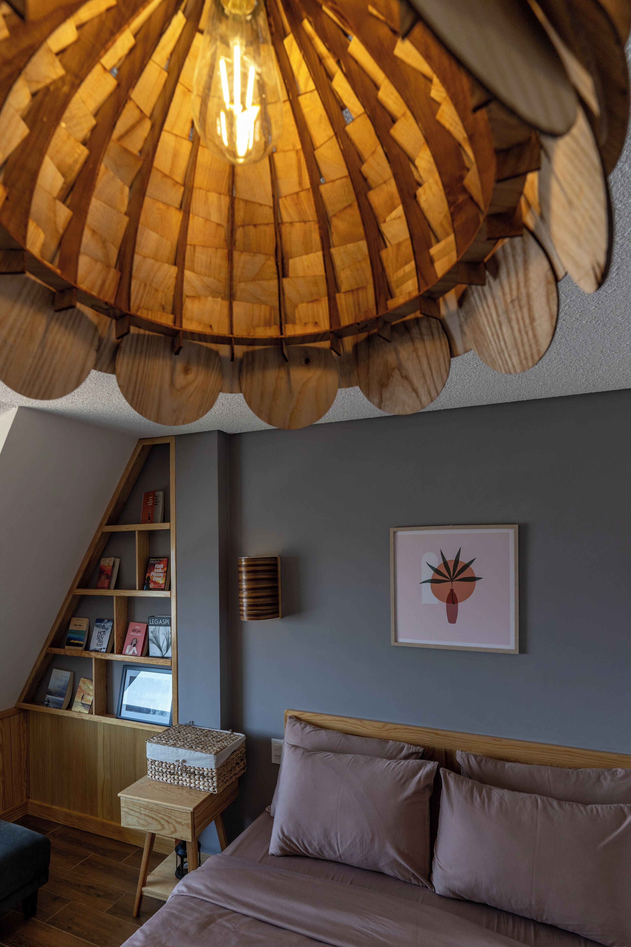 Un dormitorio con una lámpara de techo de madera, una estantería, un cuadro en la pared y una cama con almohadas.