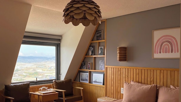 A bedroom with a large bed, a wooden headboard, a bookshelf, and a view of the landscape through a window. - View Home Da Lat (Xuan Truong - Da Lat)