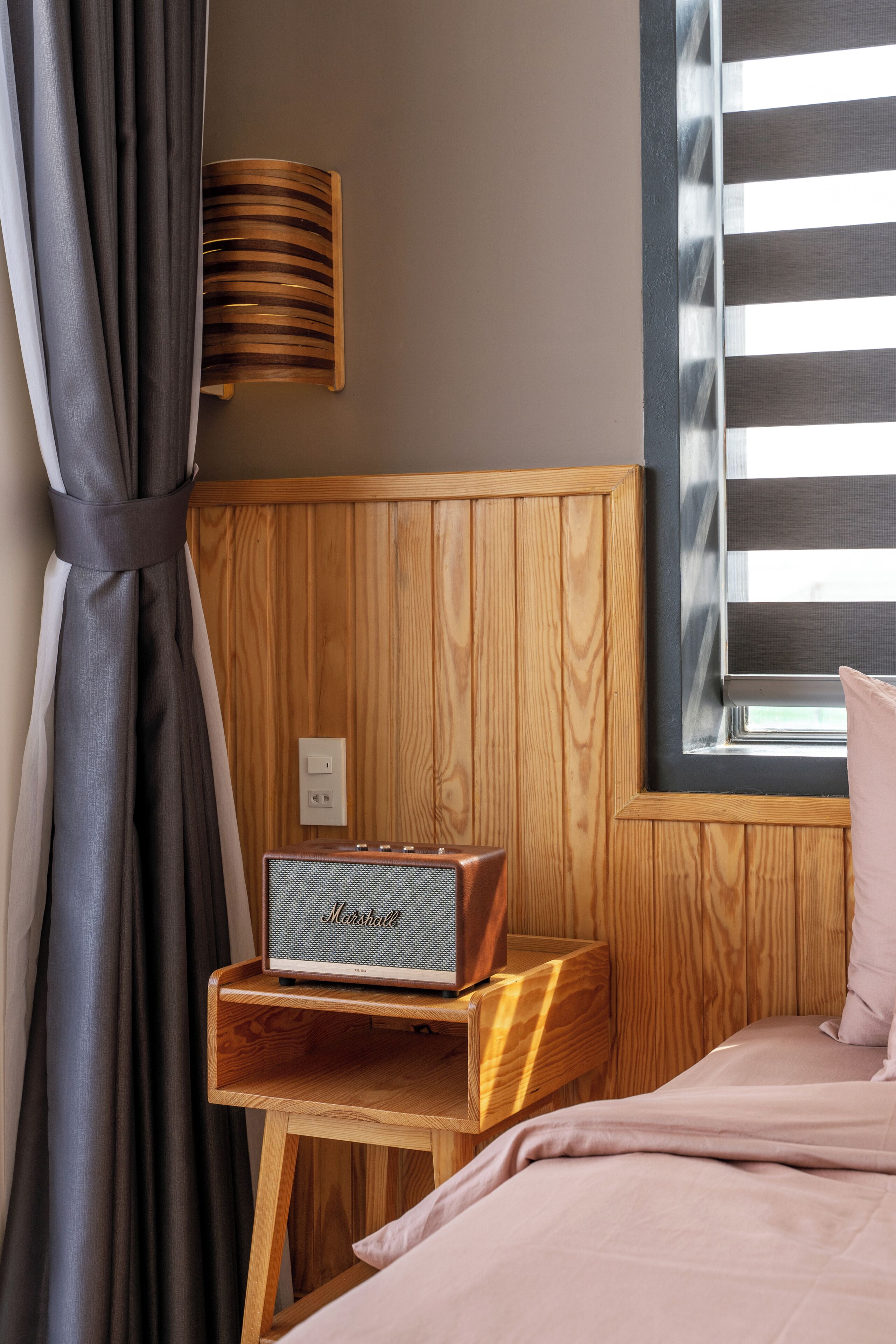 A wooden headboard with a radio, a window with blinds, and a bed with a pink pillow.
