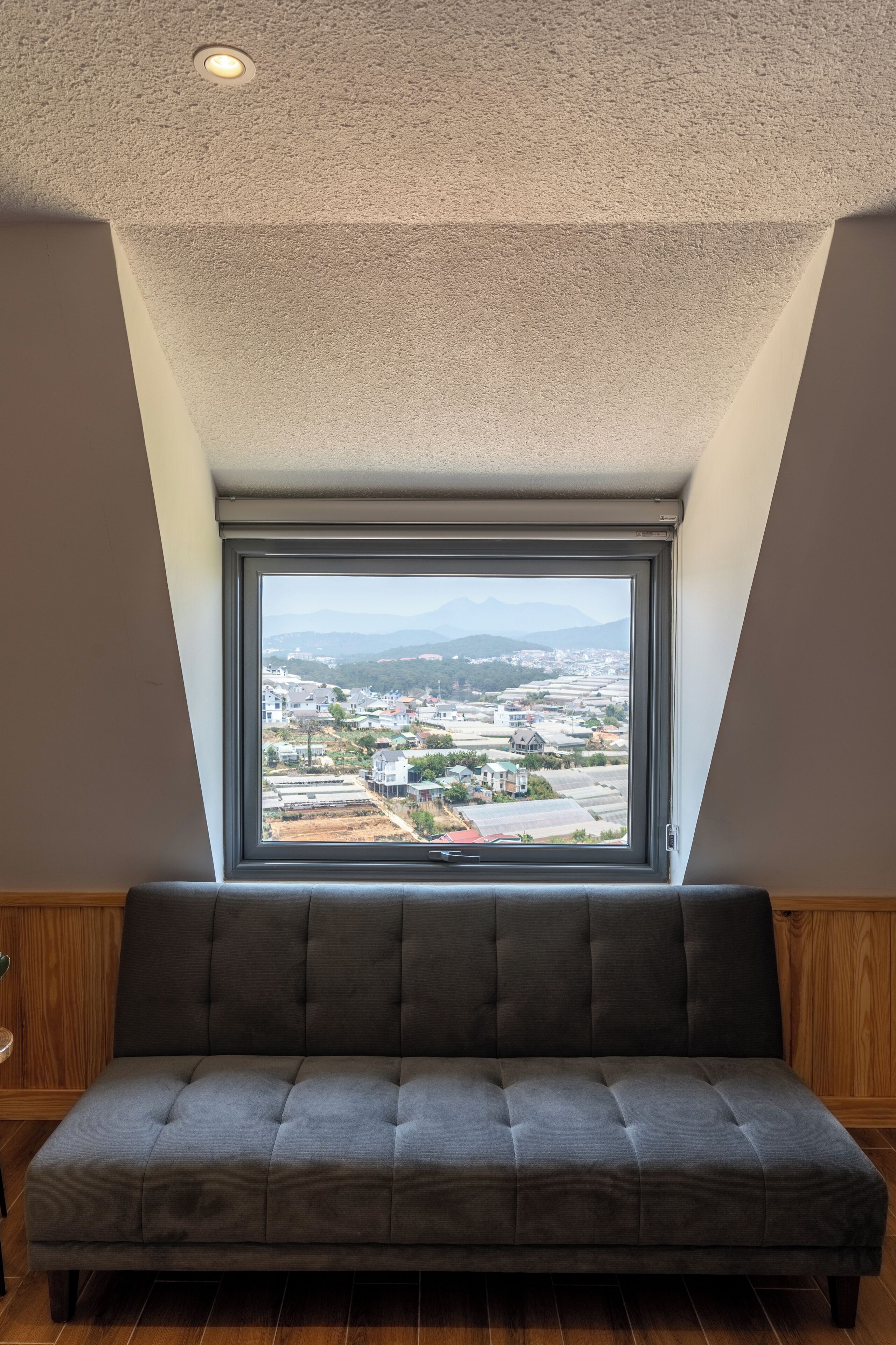 A room with a large window, a grey sofa, wooden paneling, and a textured ceiling.
