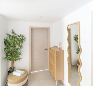 A room with a wooden cabinet, a mirror, a door, and a potted plant. - Estrella Dominicus Poolside Apartment | Atria 102 (Dominicus)