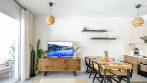 Een moderne woonkamer met een televisie, eettafel, stoelen en een keukenhoek.