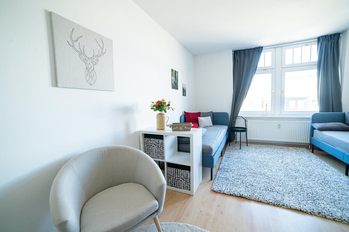A modern living room with a sofa, a chair, a small table with a vase, and a window with curtains.