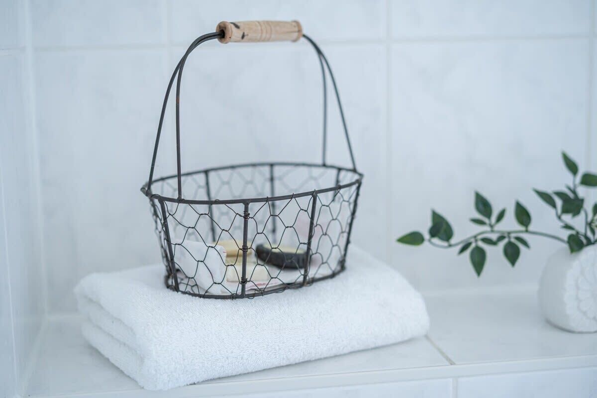 A wire basket with a wooden handle on a white tiled surface.