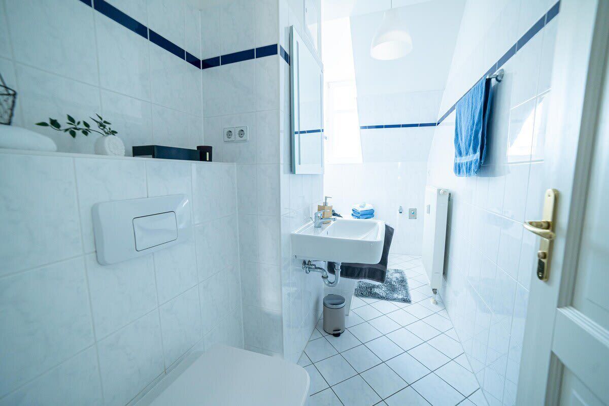 A bathroom with white tiles, a sink, a mirror, and a towel hanging on the wall.