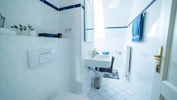 A bathroom with white tiles, a sink, a mirror, and a towel hanging on the wall.