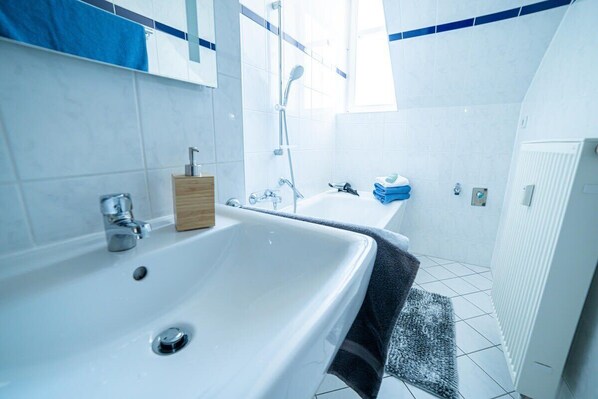 Ein modernes Badezimmer mit einer großen weißen Badewanne, einer separaten Duschkabine und einem kleinen Waschbecken.