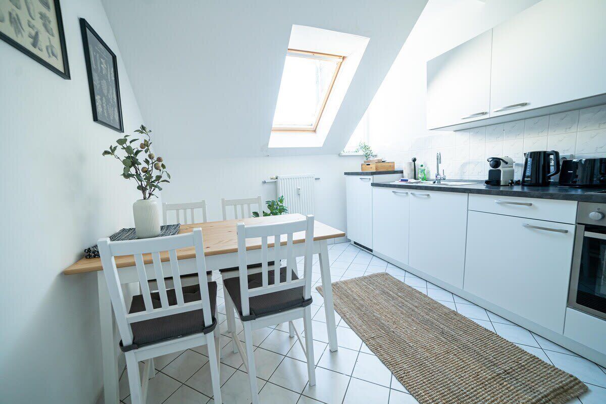 A modern kitchen with white cabinets, a dining area with a wooden table and white chairs, and a skylight above the dining table.