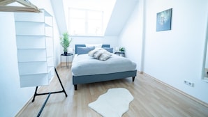 Ein modernes Schlafzimmer mit einem Bett, einer Topfpflanze, einem weißen Teppich und einem Deckenventilator.