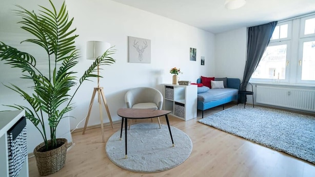 Ein modernes Wohnzimmer mit einem runden Tisch, einer Couch, einem Sessel und einer großen Topfpflanze.