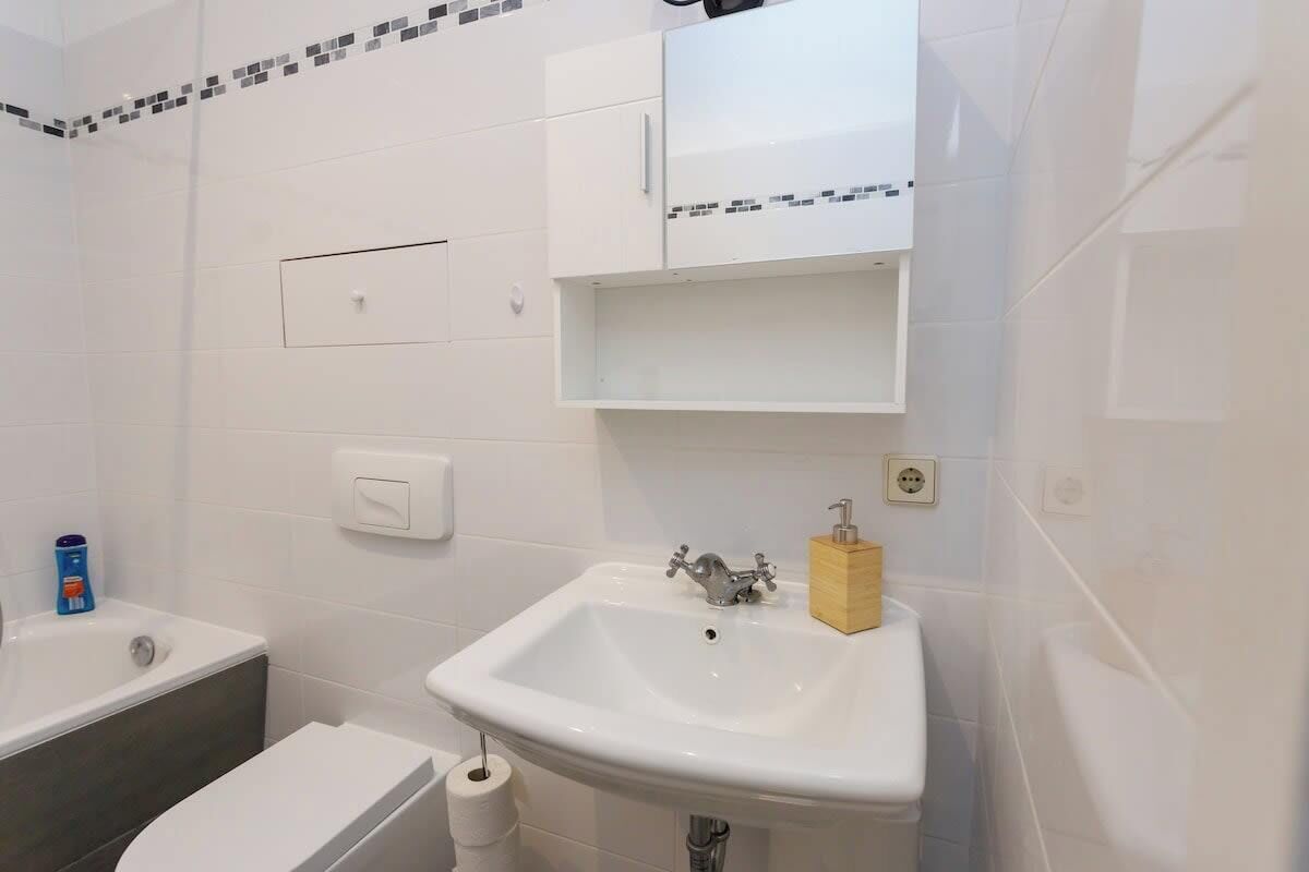 A bathroom with a white sink, a toilet, and a bathtub. There is a soap dispenser on the sink and a toilet paper roll beside the toilet.