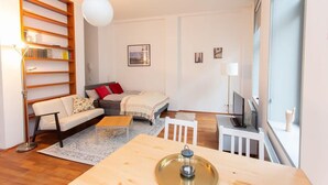 Ein modernes Wohnzimmer mit einer Couch, einem Esstisch, einem Bücherregal und einem großen Fenster.