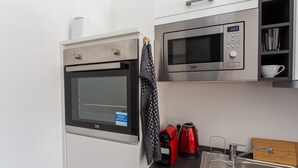 Uma cozinha compacta com forno embutido, micro-ondas e chaleira sobre a bancada.