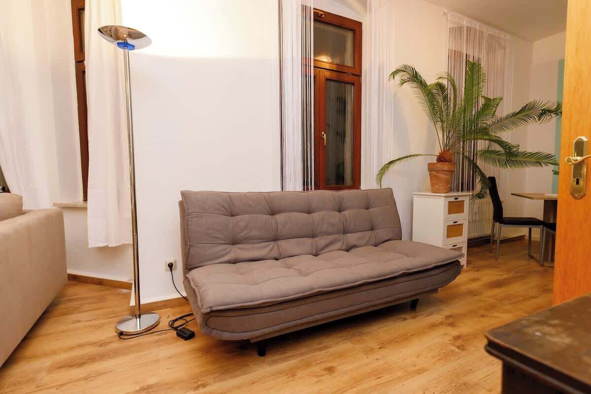 Ein Zimmer mit einer Couch, einer Stehlampe, einem Topf mit Pflanze und einer Holztür.