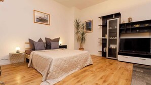 Een slaapkamer met een bed, nachtkastje, lamp en een tv-meubel met planken.