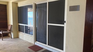 A room with a sliding glass door leading to a balcony, a wooden chair, and a doormat.