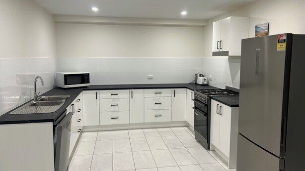 A modern kitchen with white cabinets, a black countertop, stainless steel appliances, and recessed ceiling lighting.
