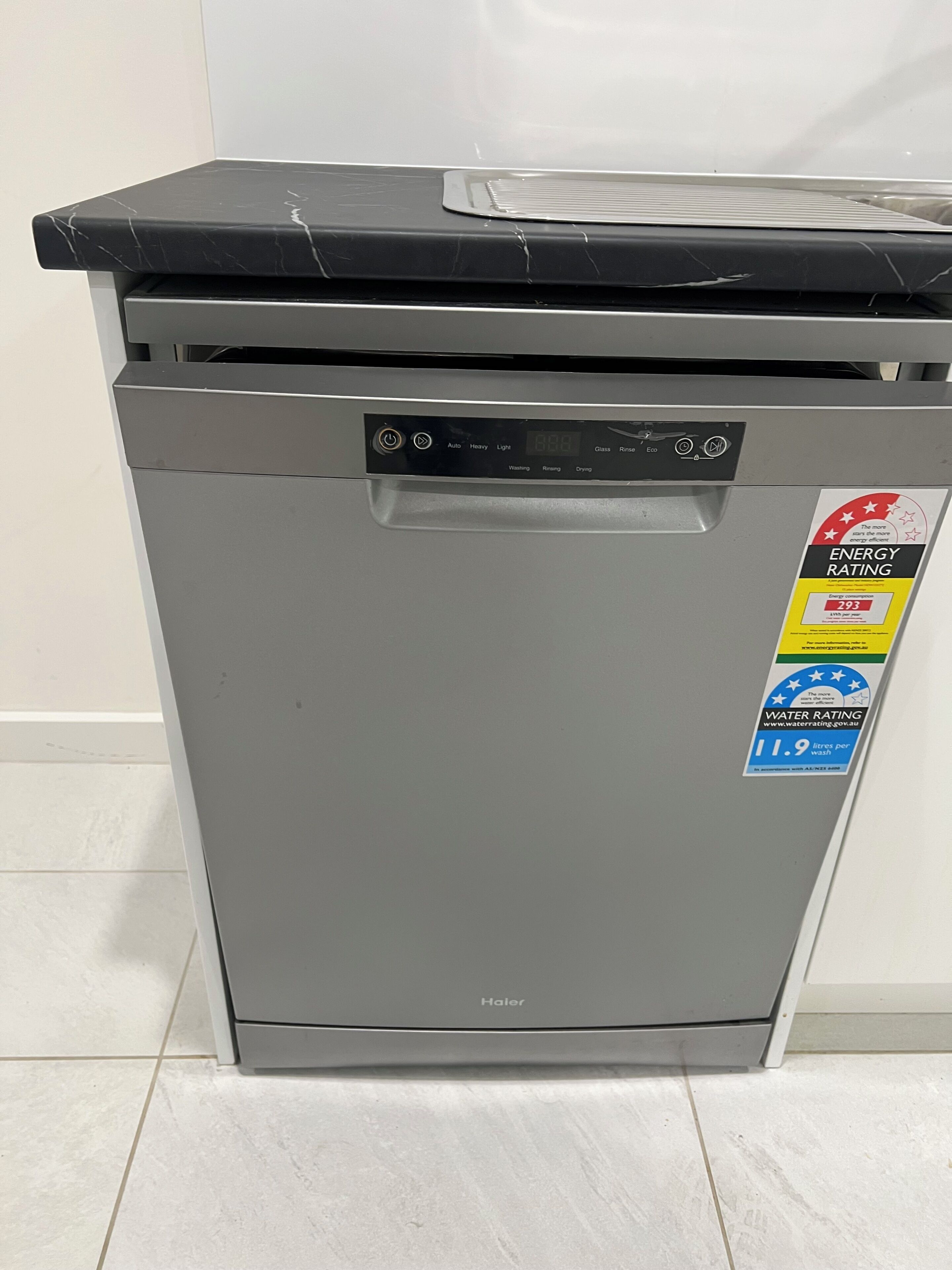 Un lave-vaisselle compact de couleur grise, avec un dessus noir, muni d’une étiquette indiquant sa classe d’efficacité énergétique et sa consommation d’eau.