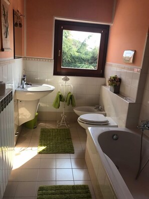 A bathroom with a window, a sink, a toilet, a bathtub, and a green rug.