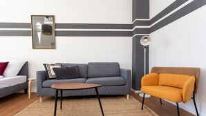 Un salon moderne avec un canapé gris, un fauteuil orange, une petite table ronde et un lampadaire.
