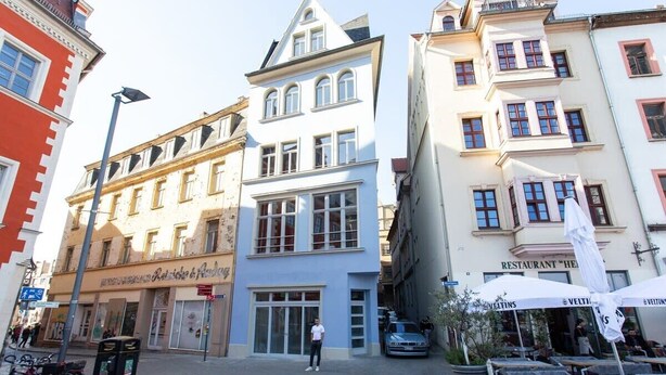 Une rue bordée d’immeubles, un homme debout et des tables installées à l’extérieur.