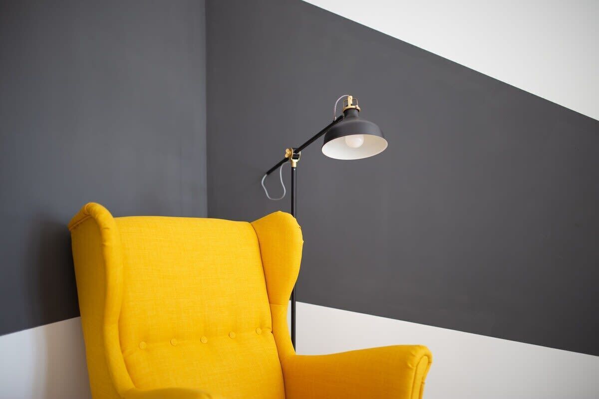 Ein gelber Sessel vor einer dunklen Wand, mit einer schwarzen Stehlampe.