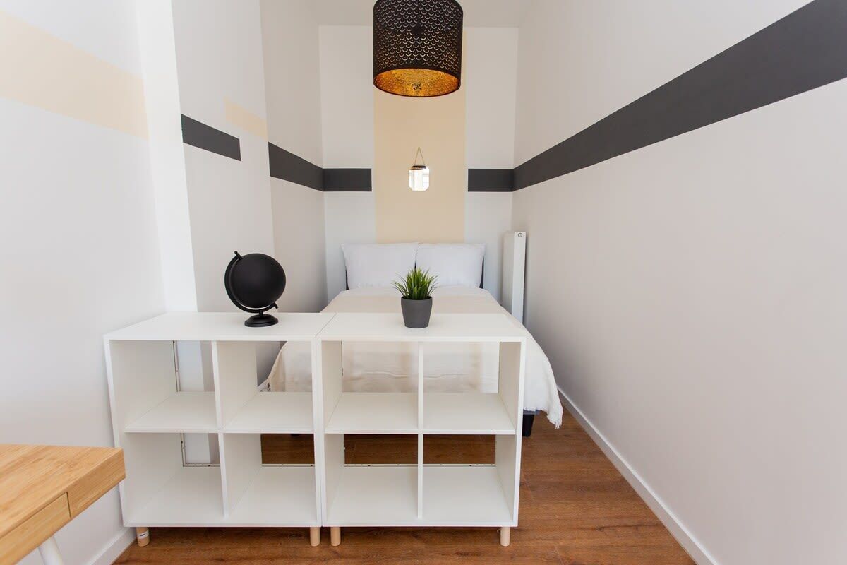 Une chambre à coucher avec un lit, une console blanche surmontée d’un globe terrestre, une plante en pot et un luminaire suspendu.