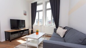 A modern living room with a grey sofa, a white coffee table, a TV on a wooden cabinet, and a window with curtains.