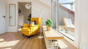 Una sala de estar moderna con un sillón amarillo, una lámpara de pie, un banco de madera y un ventanal con vistas a un balcón.