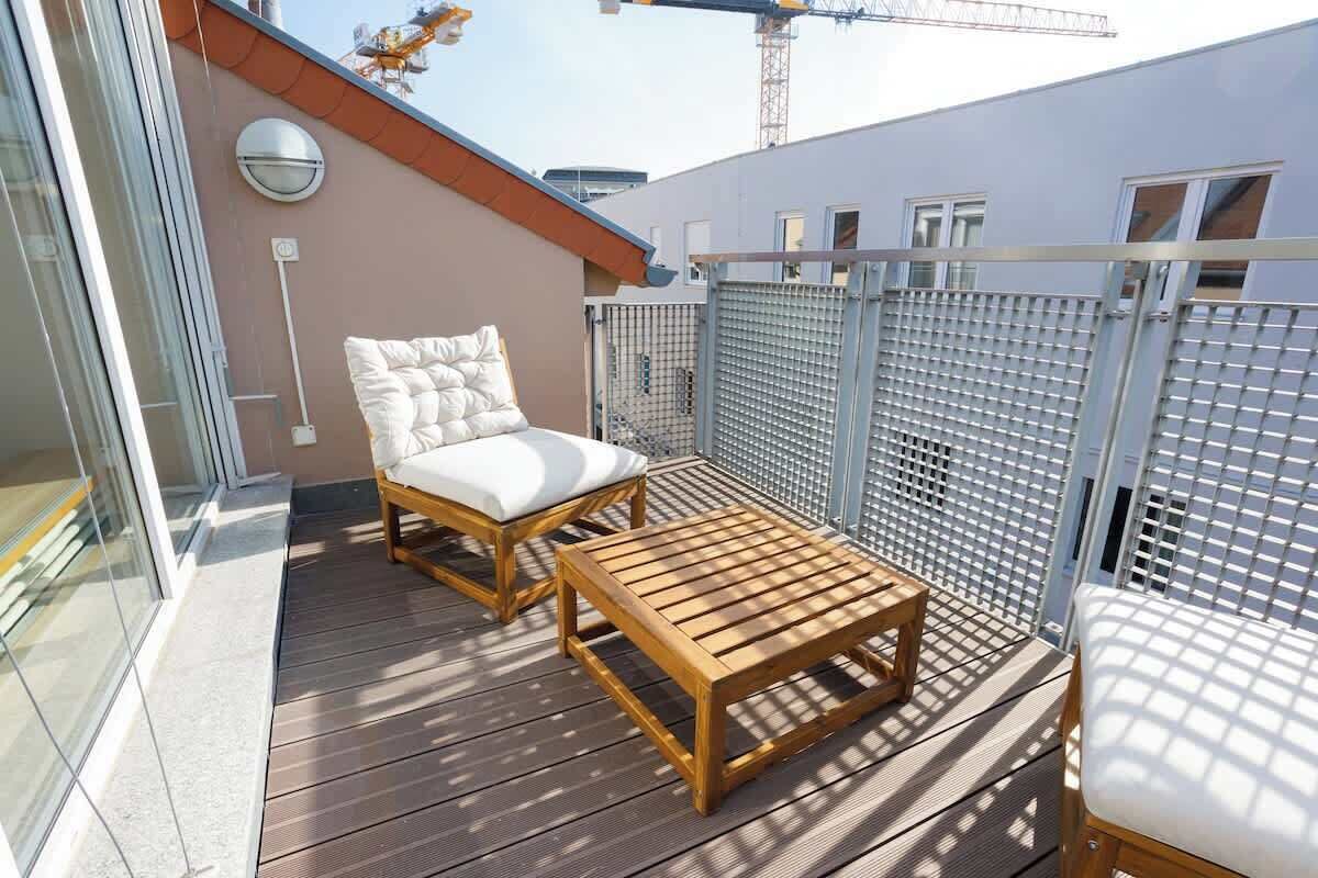 A wooden deck with a cushioned chair and a small table, enclosed by a metal fence.