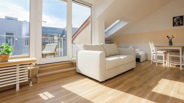 Una sala de estar moderna con un sofá blanco, una mesa de comedor y un amplio ventanal con vistas a la ciudad.