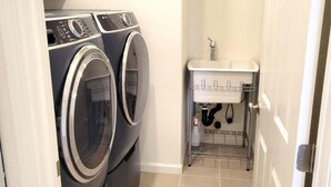 Une buanderie équipée de deux machines à laver à chargement frontal et d’un petit évier avec un étendoir en métal.