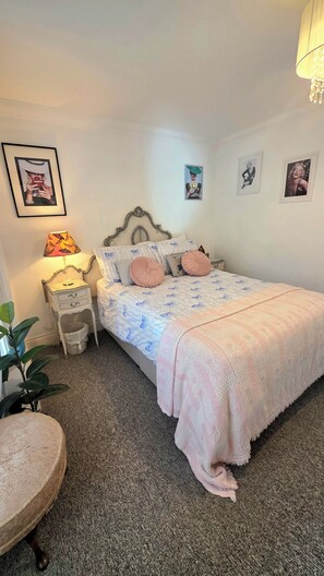 Une chambre à coucher avec un lit, des tables de chevet, une lampe, des tableaux encadrés au mur et une plante.