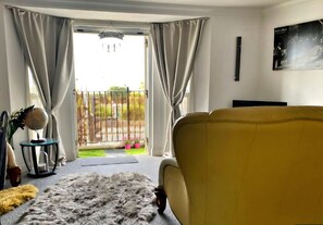 Una sala de estar con un sofá amarillo, un globo terráqueo sobre una mesita auxiliar y vistas a un patio trasero cercado.