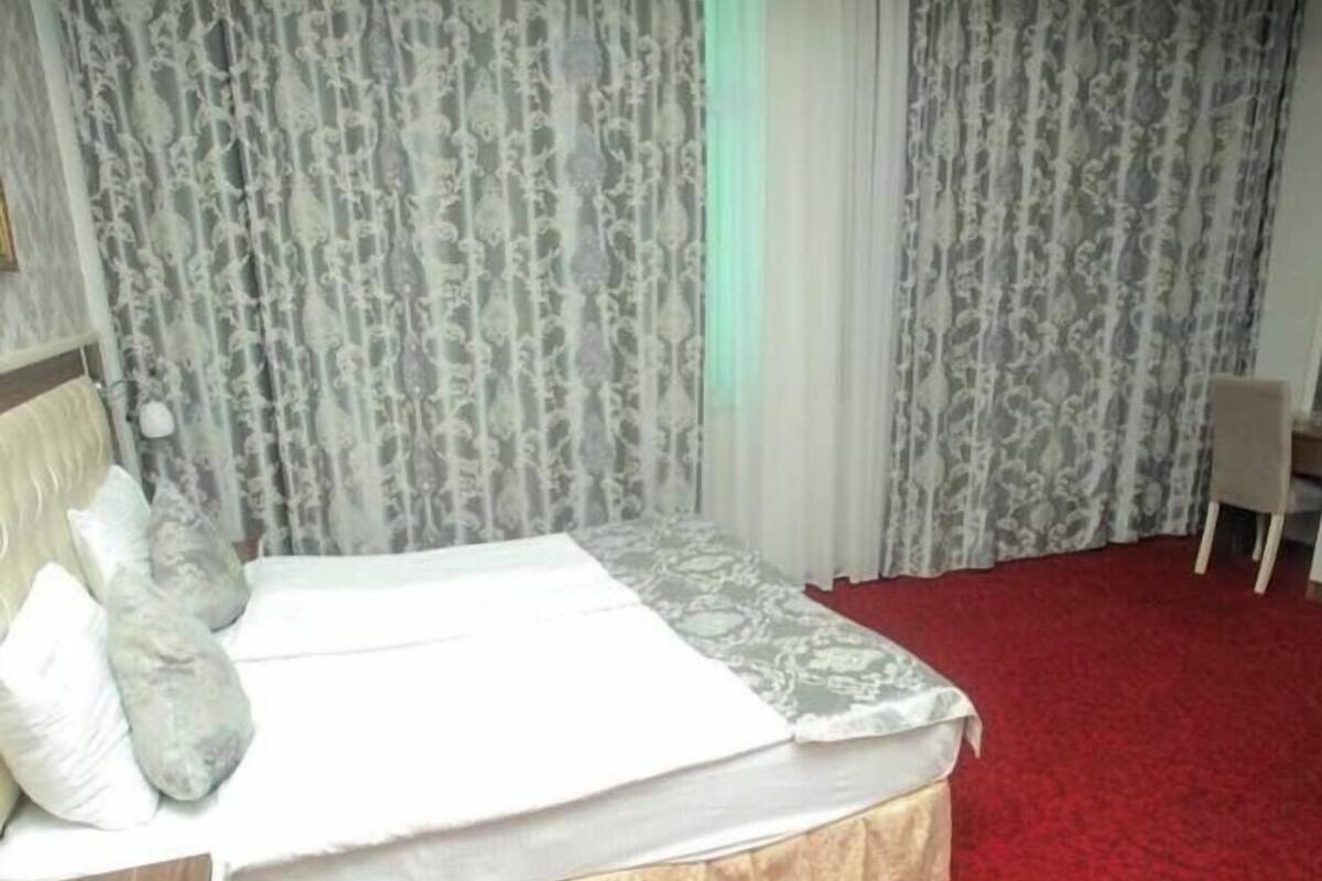 A hotel room with a bed, a wooden nightstand, a red carpet, and patterned curtains.