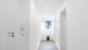 A narrow hallway with a wooden floor, white walls, a door on the left, and a window at the end. - Apartment 1 with Private Terrace, Shared Garden, and Wi-Fi (Bad Dürrheim)