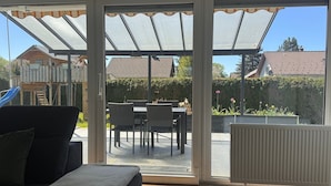 A room with a sliding glass door leading to an outdoor patio area with a table and chairs, a radiator, and a sofa with a blanket. - Apartment 1 with Private Terrace, Shared Garden, and Wi-Fi (Bad Dürrheim)