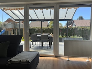 A room with a sliding glass door leading to an outdoor patio area with a table and chairs, a radiator, and a sofa with a blanket. - Apartment 1 with Private Terrace, Shared Garden, and Wi-Fi (Bad Dürrheim)