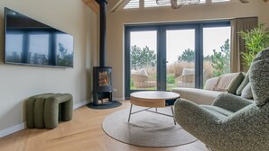 Un salon moderne avec une grande télévision, un poêle à bois, une table basse ronde et un canapé.