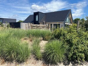 A modern house with a sloped roof, a wooden fence, and a sandy path leading to the entrance. - Charming and comfortable chalet for 4 people at Kustpark Muralt in Scharendijke, ideal for a relaxin (Scharendijke)